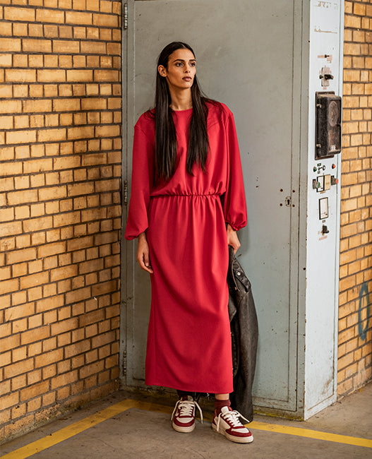 Woman wearing the Onyx Dress sewing pattern from Fibre Mood on The Fold Line. A dress pattern made in crepe, lyocell, satin, or wool fabric, featuring a relaxed fit, round neckline, elasticated waist, long sleeves with elasticated sleeve hems, and a slit at the back.
