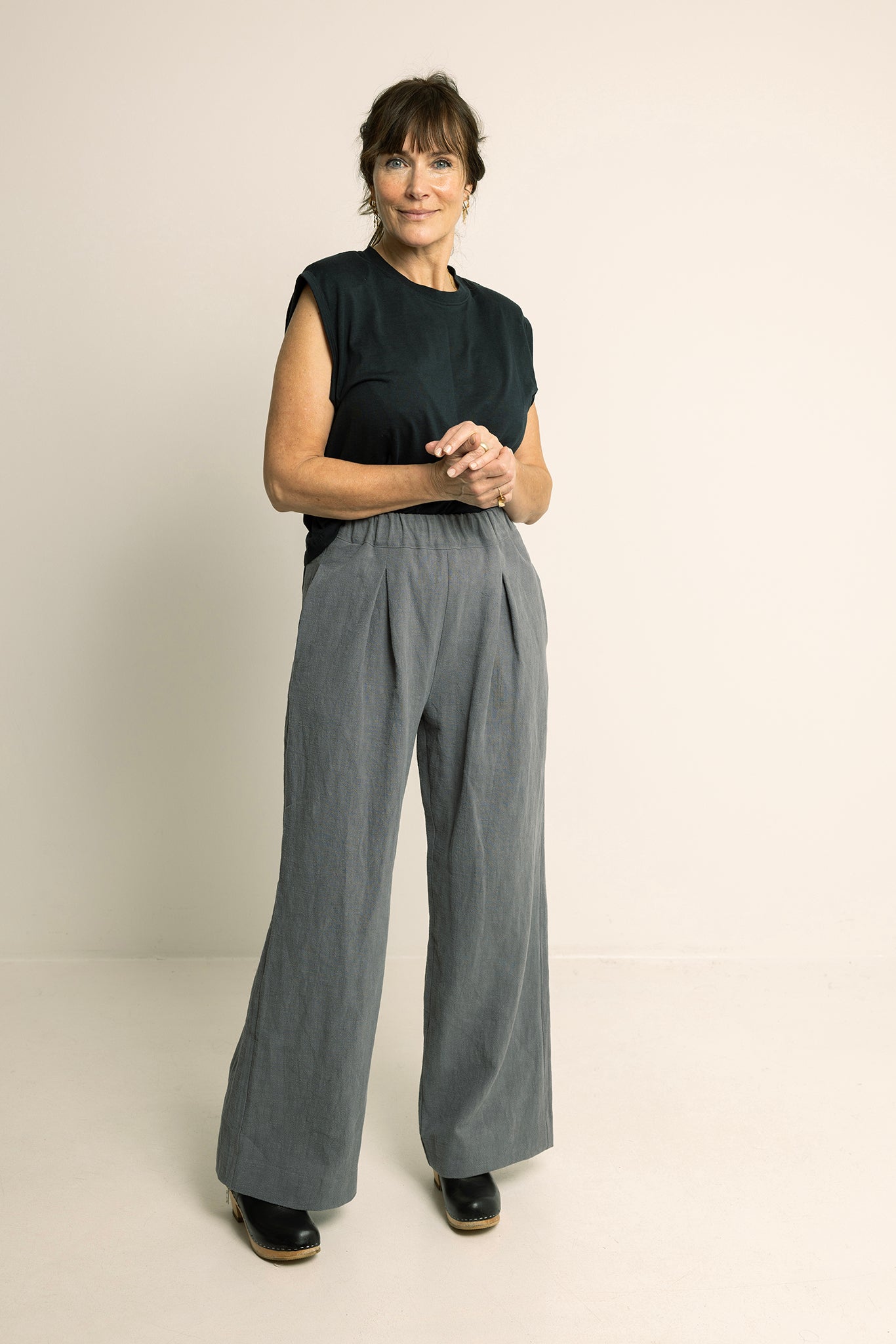 Woman wearing the Palazzo Pants sewing pattern from Wardrobe by Me on The Fold Line. A trousers pattern made in cotton, linen, viscose, denim, or corduroy fabric, featuring a relaxed fit, elastic waistline, front pleats, in-seam side pockets, back patch pockets, and wide legs.