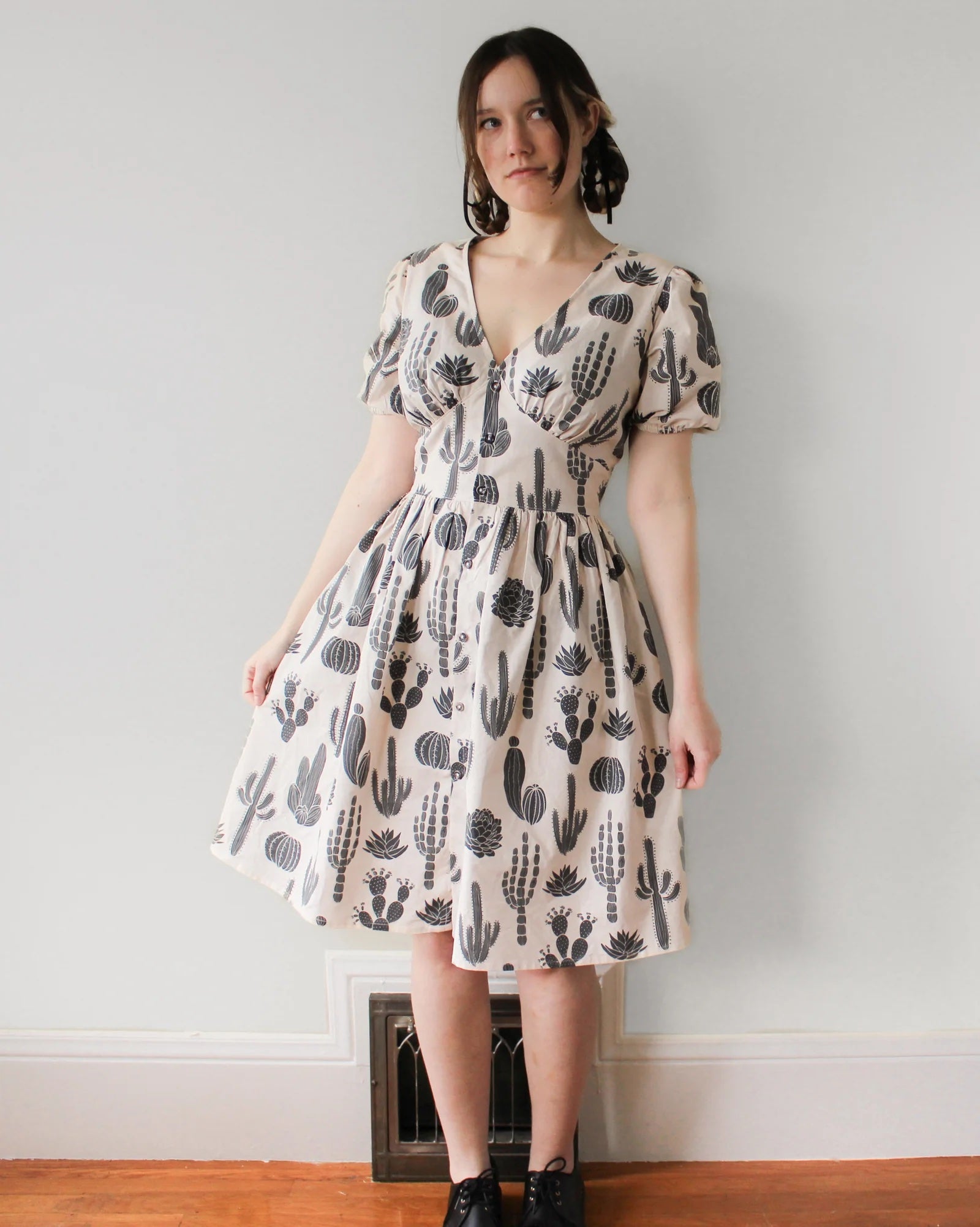 Woman wearing the Pepper Dress sewing pattern from Oh Me Oh My Sewing on The Fold Line. A dress pattern made in quilting cotton, washed linen, cotton lawn, voile, or rayon challis fabric, featuring a deep V-neckline, fitted waist panel, front button closure, short puff sleeves, gathered skirt, and knee length.