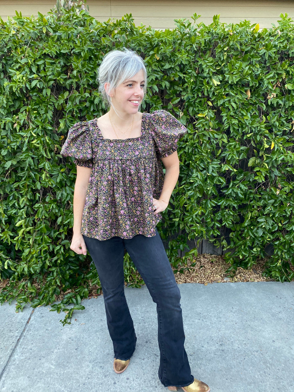 Woman wearing the Polly Blouse sewing pattern from Daisy Chain Patterns on The Fold Line. A smock top pattern made in cotton lawn or poplin or lightweight linen fabric, featuring a square neckline with a ruffle and short puff sleeves.