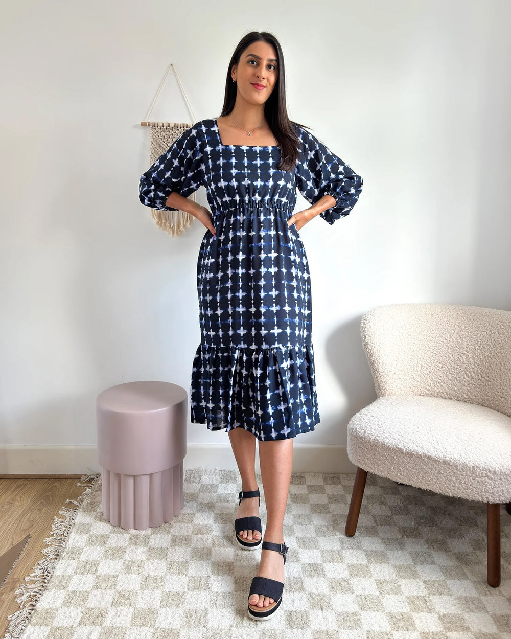 Woman wearing the Raj Dress sewing pattern from Tammy Handmade on The Fold Line. A dress pattern made in cotton, linen, viscose, crepe, or satin fabric, featuring a square neckline, elasticated waist, 3/4 length sleeves, and a gathered ruffle at the hem.