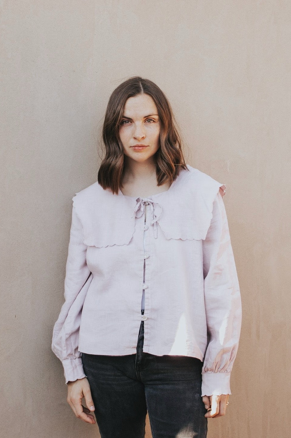 Woman wearing the Rosamund Blouse sewing pattern from Madswick on The Fold Line. A blouse pattern made in linen, viscose, tencel, chambray, cotton lawn, cotton poplin, silk, or cotton twill fabric, featuring a square neckline with a sailor collar, button-up front with button loops, and long gathered sleeves with loose cuffs.