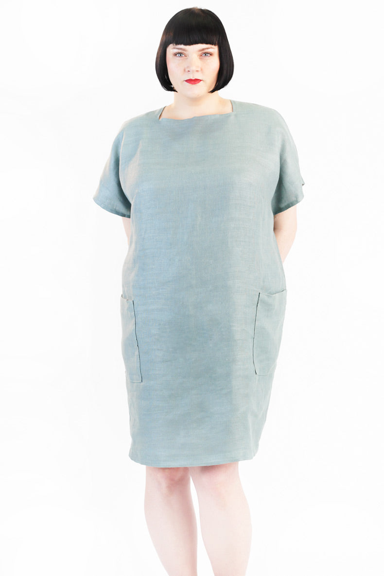 Woman wearing the Rose Dress sewing pattern from Schnittchen Patterns on The Fold Line. A knee-length dress pattern made in linen, viscose, or cotton fabric, featuring a relaxed fit, bateau neckline with triangle inserts, short sleeves, and patch pockets.