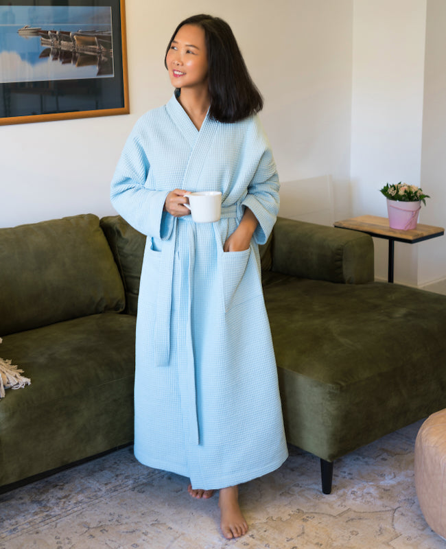 Woman wearing the Roseto Robe sewing pattern from Itch to Stitch on The Fold Line. A dressing gown pattern made in terry cloth, waffle knit, fleece-backed French terry, flannel, or silk satin fabric, featuring ample ease, dropped shoulders, a sash and belt loops, patch pockets, and an ankle length.