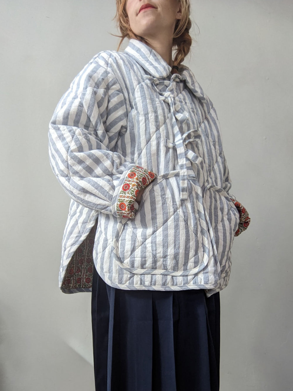 Woman wearing the Rue Quilt Coat sewing pattern from Spaghetti Western Sewing on The Fold Line. A quilted jacket pattern made in quilting cotton, linen, pre-quilted fabric, or upcycled blankets, featuring a relaxed oversized fit, dropped shoulders, collar, side splits, patch pockets, and tie closures.