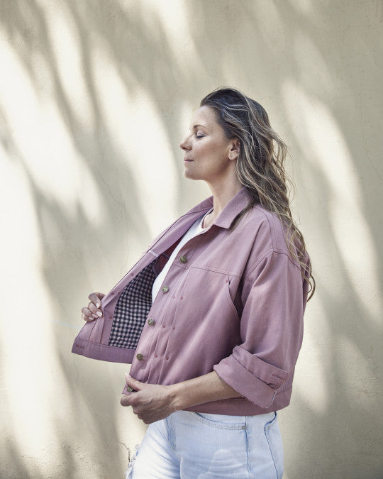 Woman wearing the Russafa Jacket sewing pattern from Pauline Alice on The Fold Line. A jacket pattern made in denim, cotton canvas or twill, or corduroy fabric, featuring a relaxed fit, lapel collar, front button closure, pleats at the front and back, a front patch pocket, big side pockets, long sleeves with cuffs, a cinch back, and cropped length.