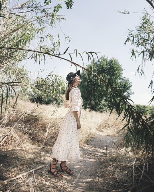 Woman wearing the Sedavi Dress sewing pattern from Pauline Alice on The Fold Line. A dress pattern made in cotton lawn, batiste, silk, twill, crepe, or viscose fabric, featuring a fitted bodice framed by knife pleats, elbow length sleeves with a ruffled hem, and a long full skirt finished with a gathered tier.