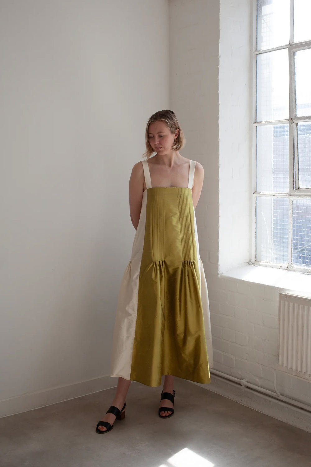 Woman wearing the Sienna Dress sewing pattern from The Modern Sewing Co. on The Fold Line. A dress pattern made in linen, cotton lawn/poplin, raw silk, viscose, silk taffeta, or silk satin fabric, featuring wide straps, pleated panels, side pockets, and a midi length.