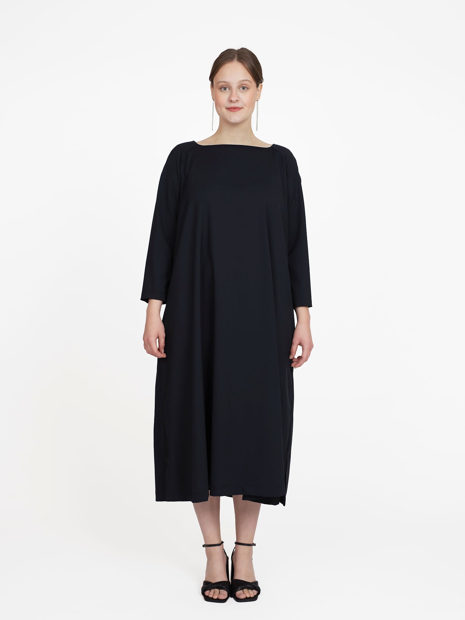 Woman wearing the Square Neck Dress sewing pattern from The Assembly Line on The Fold Line. A dress pattern made in wool or cotton fabric, featuring an A-line shape, bracelet length raglan sleeves, side seam pockets, side slits at the hem, and a midi length.