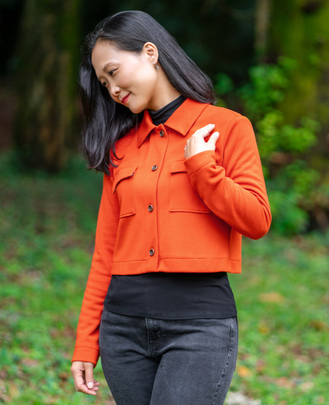 Woman wearing the Teifi Cardigan sewing pattern from Itch to Stitch on The Fold Line. A cardigan pattern made in interlock, double knit, or sweater knit fabric, featuring a classic collar, button front, chest pockets with flaps, long sleeves, and cropped length.
