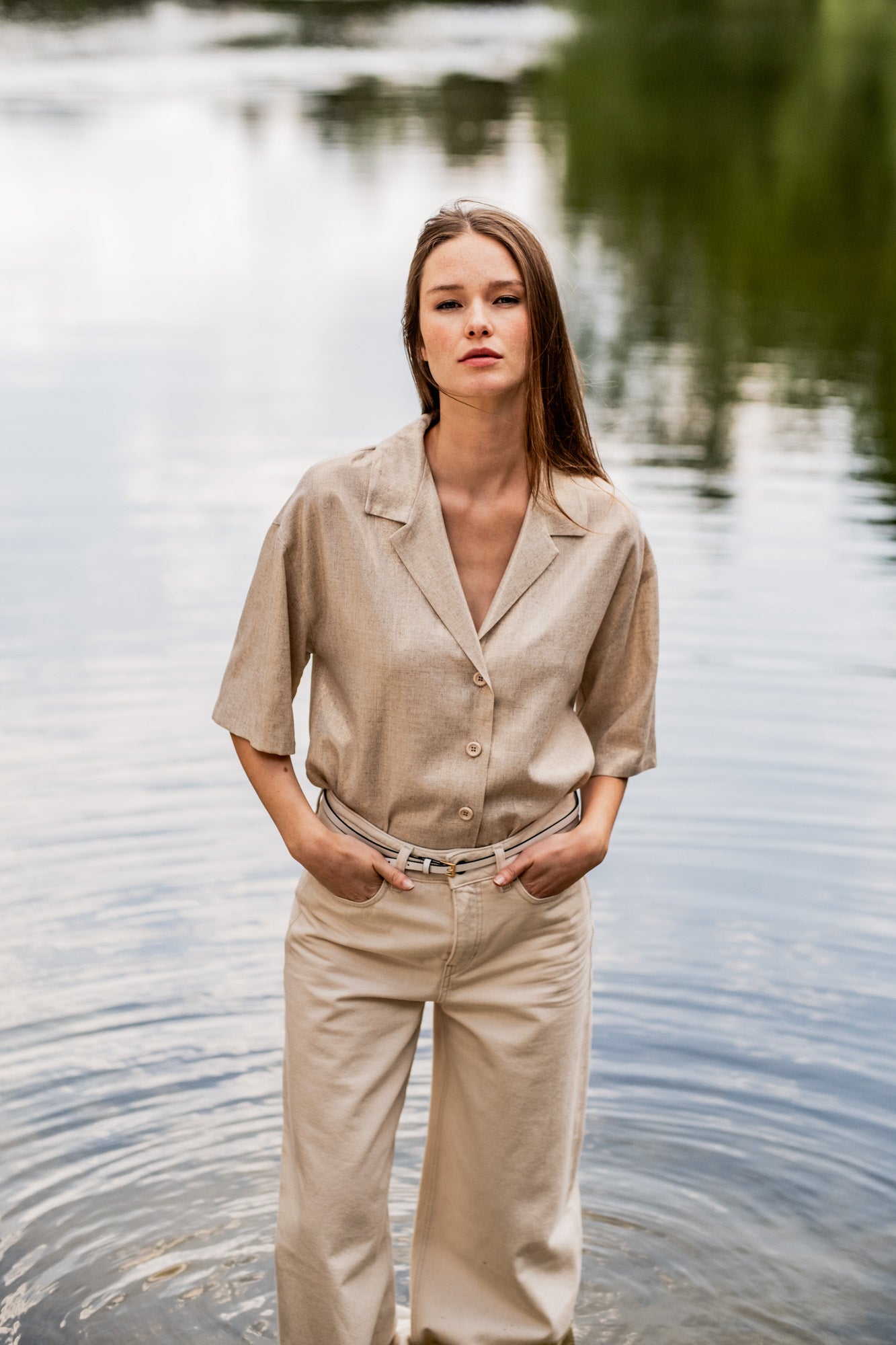 Woman wearing the Tesni Blouse sewing pattern from Fibre Mood on The Fold Line. A shirt pattern made in poplin, linen, double gauze, chambray, seersucker, or crochet fabric, featuring a deep V-neckline, collar, button front, and mid-length sleeves.