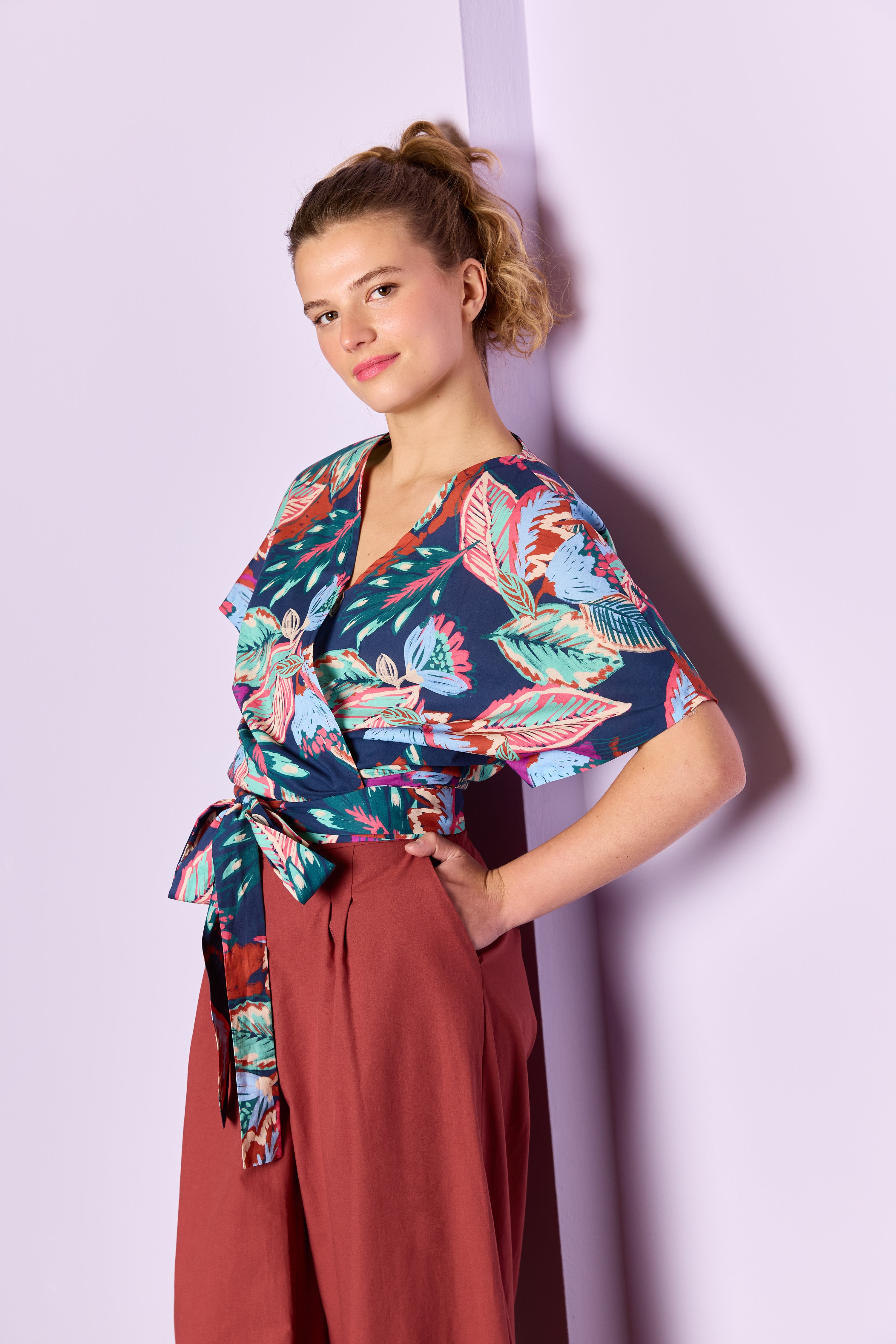 Woman wearing the Trixie Blouse sewing pattern from Atelier Jupe on The Fold Line. A top pattern made in viscose, cotton, linen, tencel, double gauze, or polyester fabric, featuring a wrap front, V-neckline, short cut-on sleeves, and a waist tie.