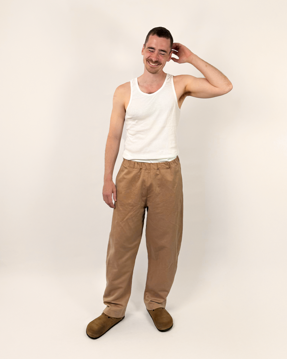 Man wearing the Unisex Volumen Pants sewing pattern from Wardrobe by Me on The Fold Line. A trousers pattern made in cotton, linen, denim, corduroy, or canvas fabric, featuring an elastic waist, side and back pockets, curved side seam, and barrel leg.