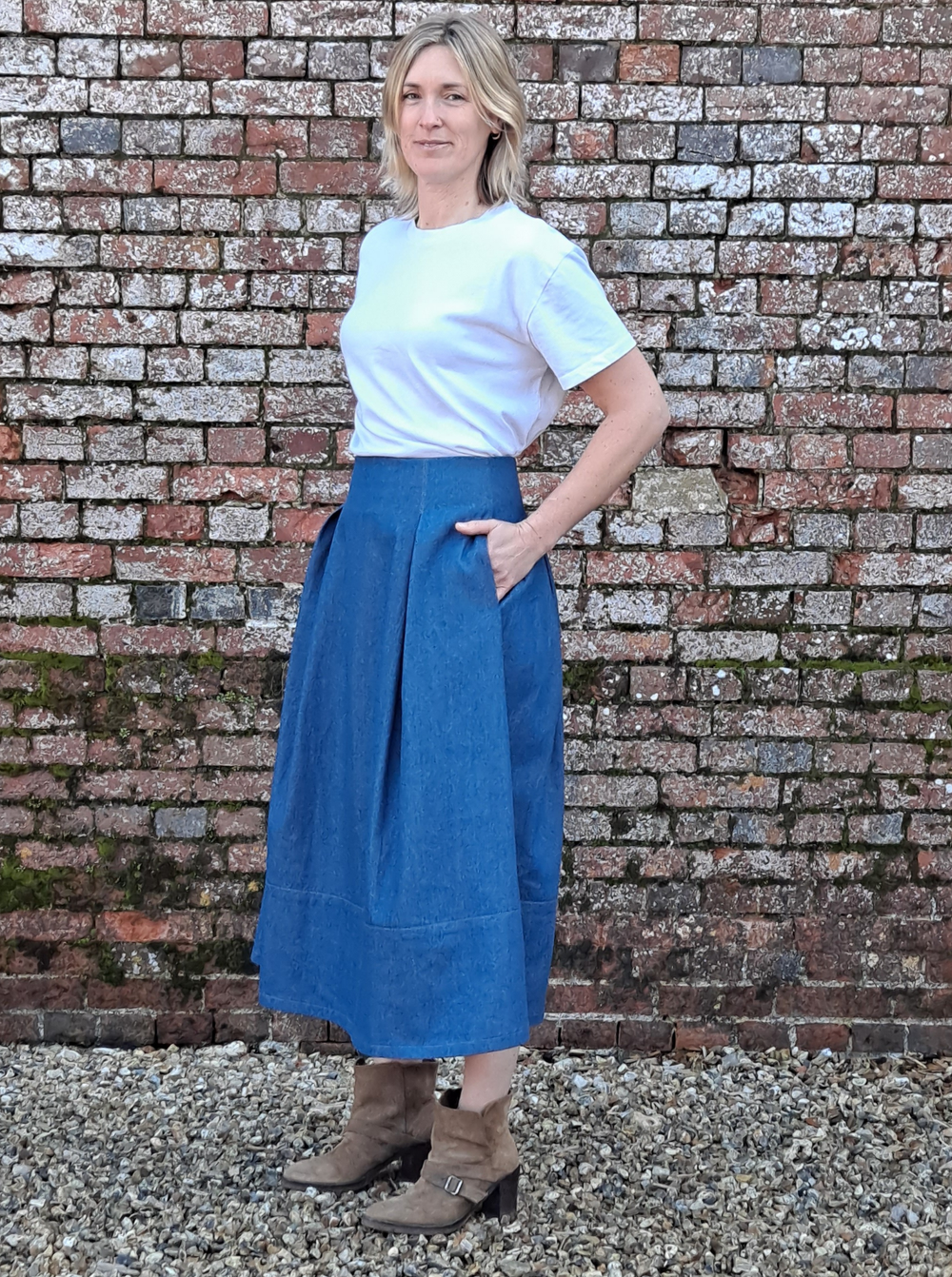 Woman wearing the Universal Skirt sewing pattern from The Avid Seamstress on The Fold Line. A skirt pattern made in cotton, linen, viscose, wool, poplin, chambray, or needlecord fabric, featuring a high waist, deep pleats, pockets, hem panel, and midi length.