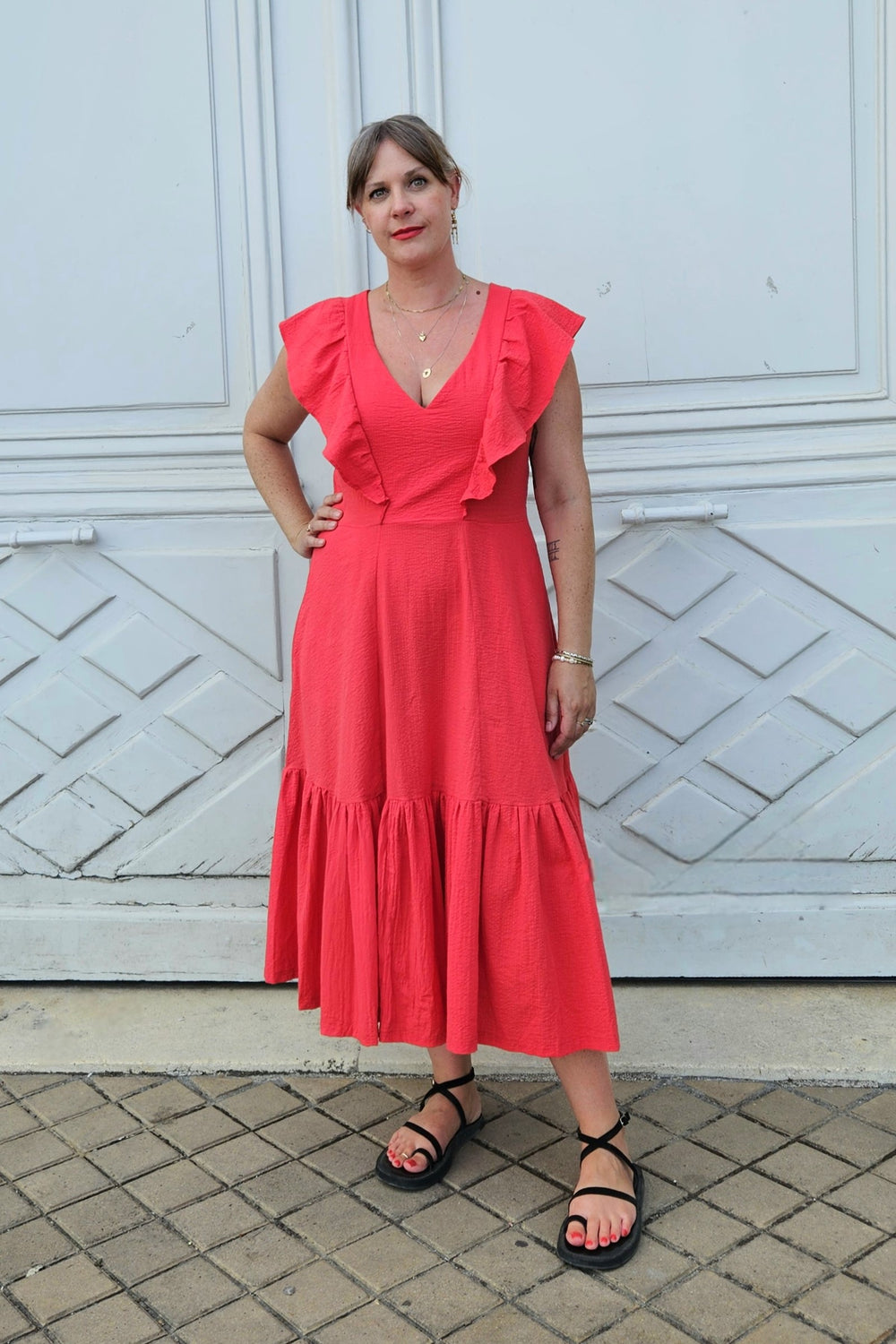 Woman wearing the Valentina Dress sewing pattern from Emporia Patterns on The Fold Line. A sleeveless dress pattern made in cotton poplin or lawn, cotton viscose blend, linen/ramie or blends, cotton sateen, seersucker, lightweight jacquard, double gauze, chambray, or viscose satin fabric, featuring a V-neck, frills that cover the shoulders, princess seams, bound armholes, and a panelled skirt with pockets and a ruffle.