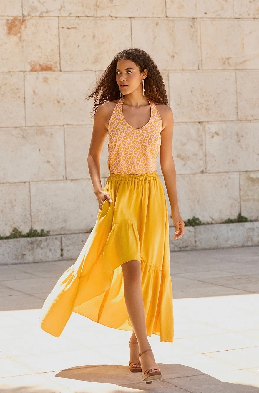 Woman wearing the Valeria Skirt sewing pattern from The Patterns Room on The Fold Line. A skirt pattern made in viscose, tencel, crepe, or satin fabric, featuring a relaxed fit, elasticated waist, and high-low high hemline with a gathered ruffle.