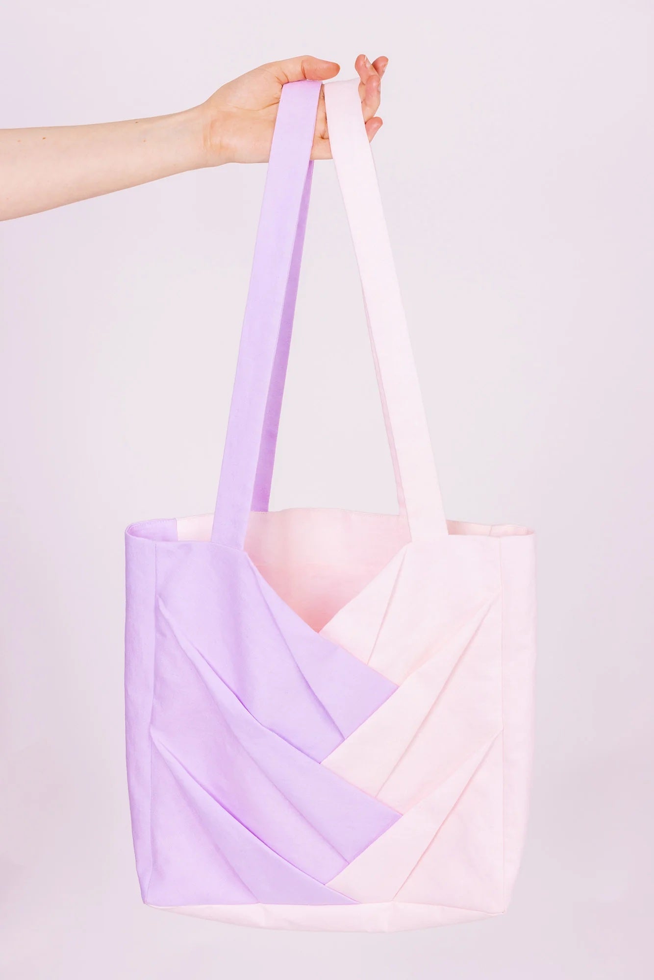 Person holding the Xenta Tote Bag sewing pattern from Forget-me-not Patterns on The Fold Line. A tote bag pattern made in medium weight woven fabric, featuring interlocking box pleats, side gussets, an internal pocket, and lining.