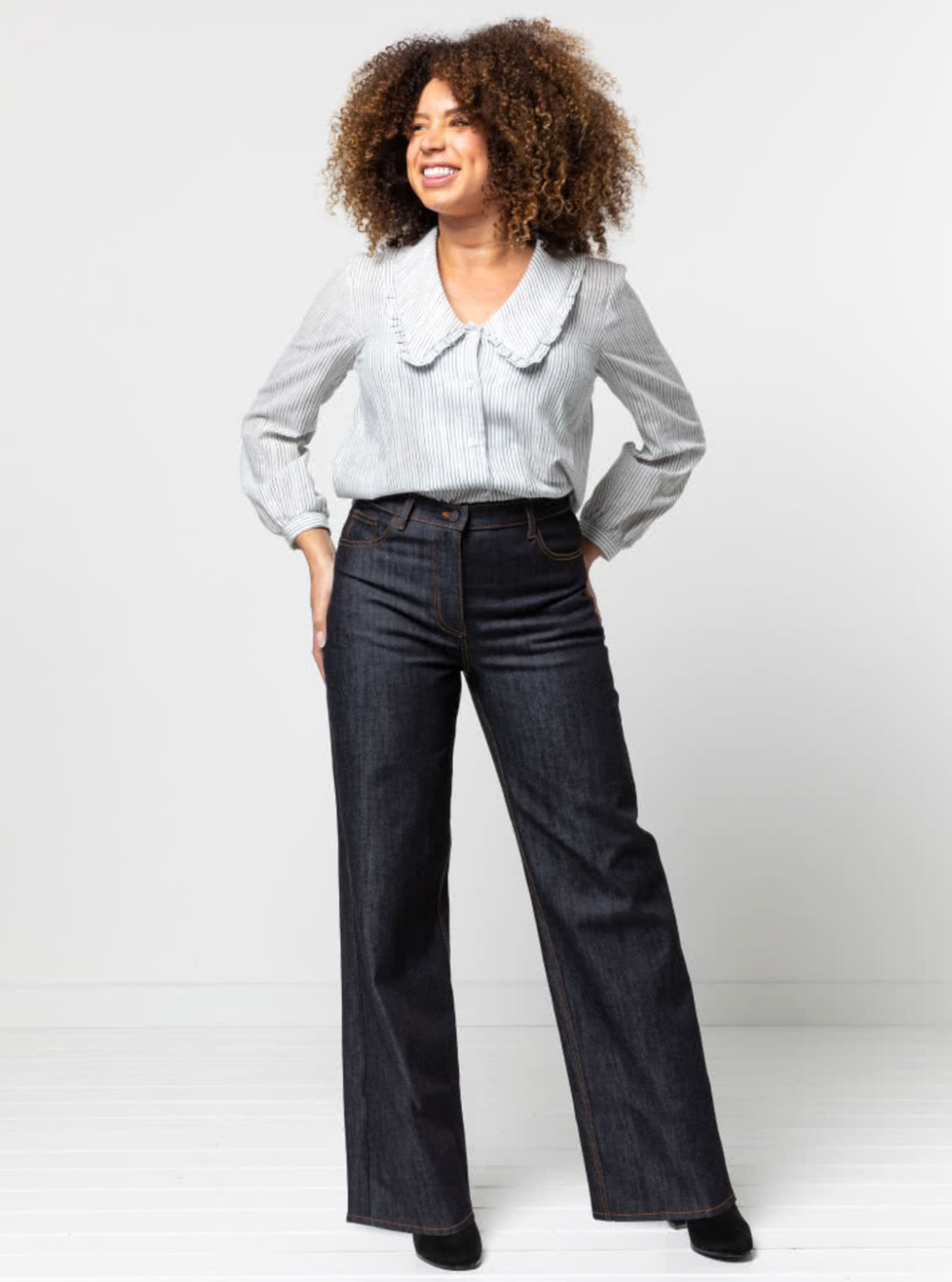 Woman wearing the Carlisle Jean sewing pattern from Style Arc on The Fold Line. A jeans pattern made in denim or cotton drill fabrics, featuring a shaped waistband, back yoke, two back patch pockets, coin pocket, wide straight leg, belt loops and fly zip
