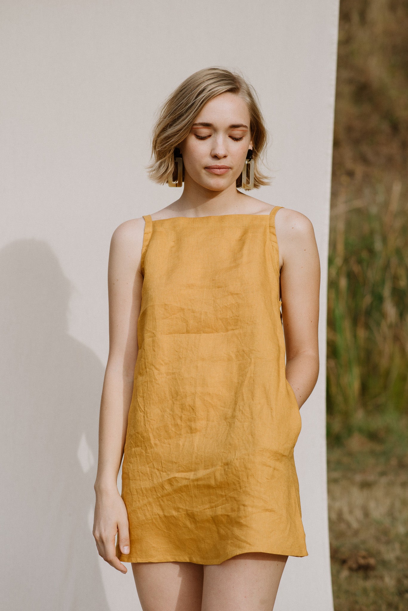 Woman wearing the Wattlebird Dress sewing pattern by Common Stitch. A strappy dress pattern made in linen fabrics, featuring spaghetti straps, front pockets and relaxed fit.