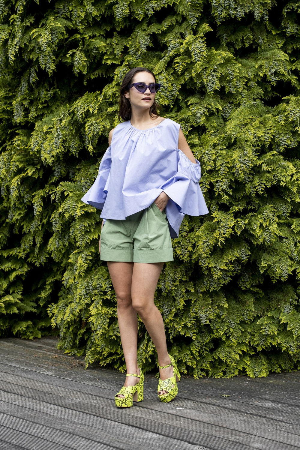 Woman wearing the Dahlia Shorts sewing pattern from Fibre Mood on The Fold Line. A shorts pattern made in twill, poplin, denim, linen, or woven jacquard fabrics, featuring a high waist with pleats, wide legs with cuffs, side slash pockets, buttoned waistb