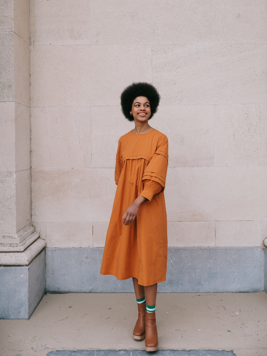 Woman wearing the Dila Dress sewing pattern from Notches on The Fold Line. A dress pattern made in cotton poplin, linen, thin wool, or viscose fabric, featuring a round neck, long lantern sleeve with pleats, gathered bodice, and midi length.