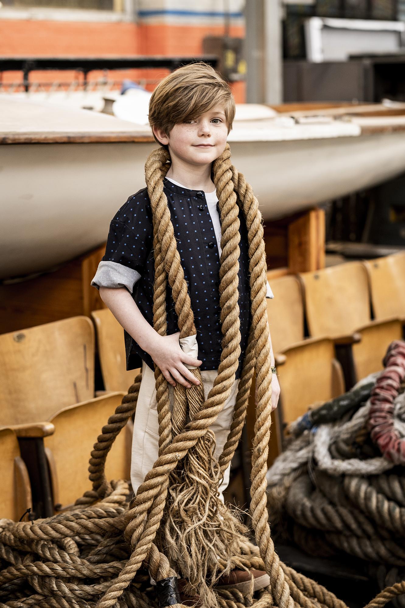 Child wearing the Child/Teen Rupert Shirt sewing pattern from Fibre Mood on The Fold Line. A shirt pattern made in poplin, chambray, Tencel, linen, crêpe, and flannel fabrics, featuring an oversized fit, standing collar, curved-hem with side slits, chest