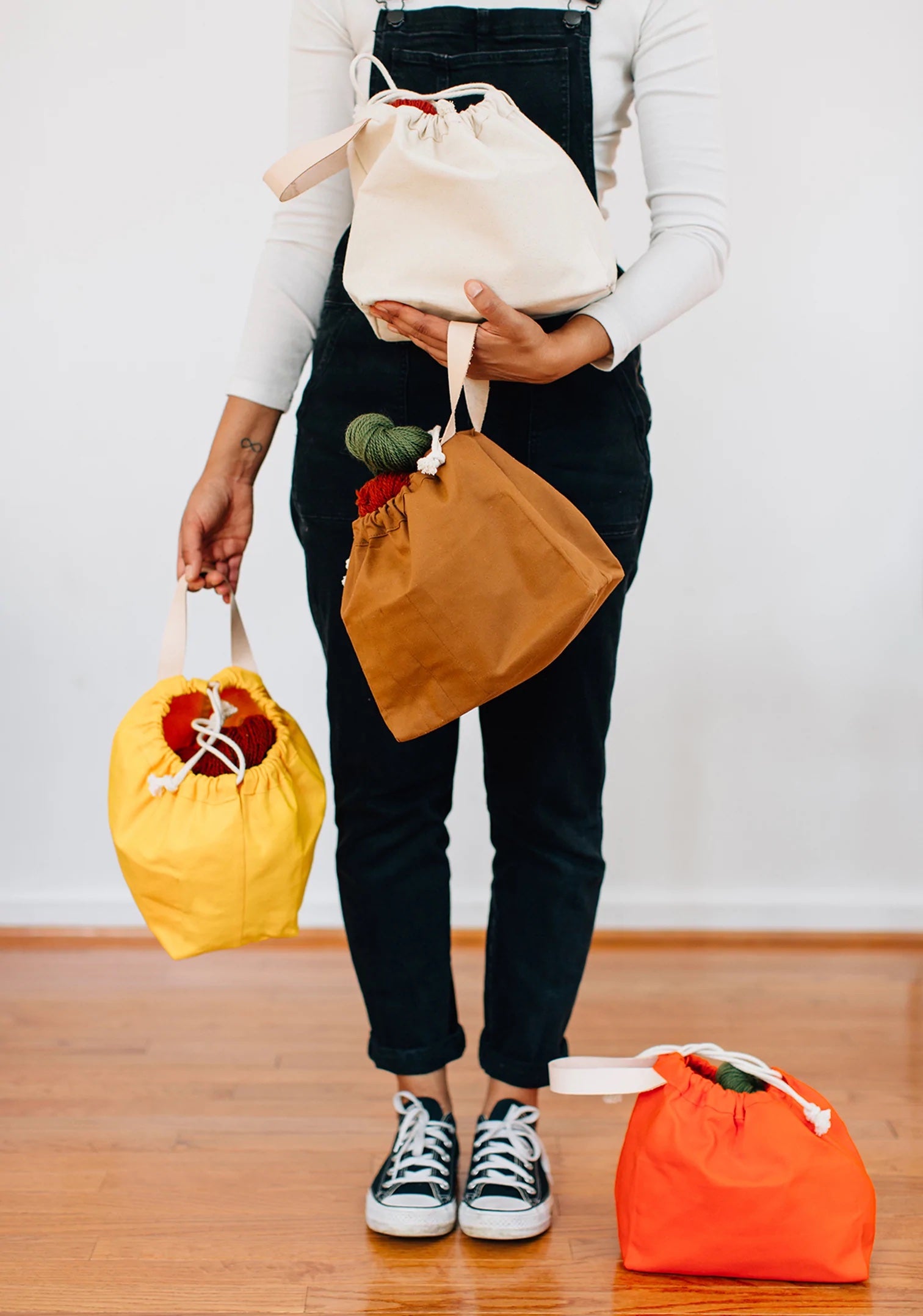 Women holding the Field Bag sewing pattern from Grainline Studio on The Fold Line. A bag pattern made in cotton canvas fabrics, featuring a roomy main compartment, interior pockets, braided cord drawstring closure and wrist strap.