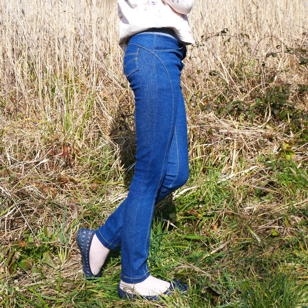 Child wearing the Child/Teen Gotan Jeggings sewing pattern from Petits D'om on The Fold Line. A jeggings pattern made in stretch denim, stretch cotton, or stretch velvet fabrics, featuring a skinny fit, back patch pockets, front slash pockets, elasticated