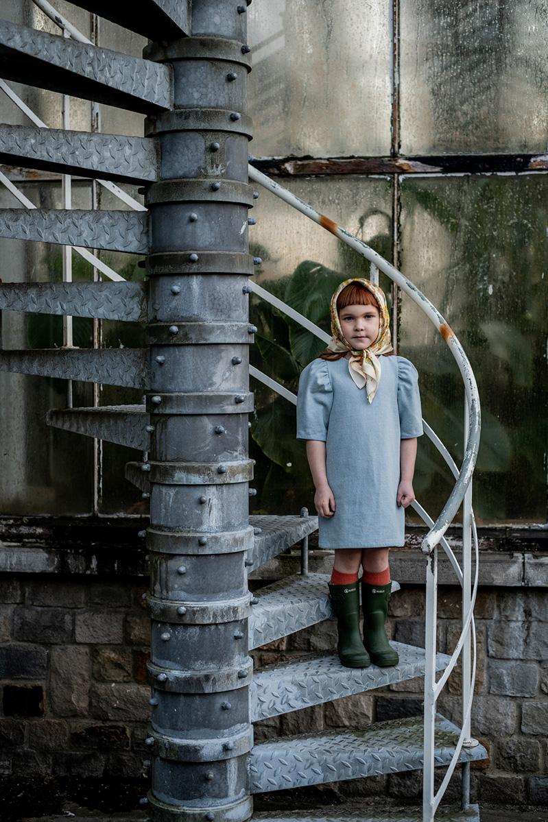 Child wearing the Child/Teen Iris Dress sewing pattern from Fibre Mood on The Fold Line. A dress pattern made in corduroy, denim, poplin, viscose (crepe), lyocell or satin fabrics, featuring elbow length puffed sleeves, back hook-and-eye, round neck, stra