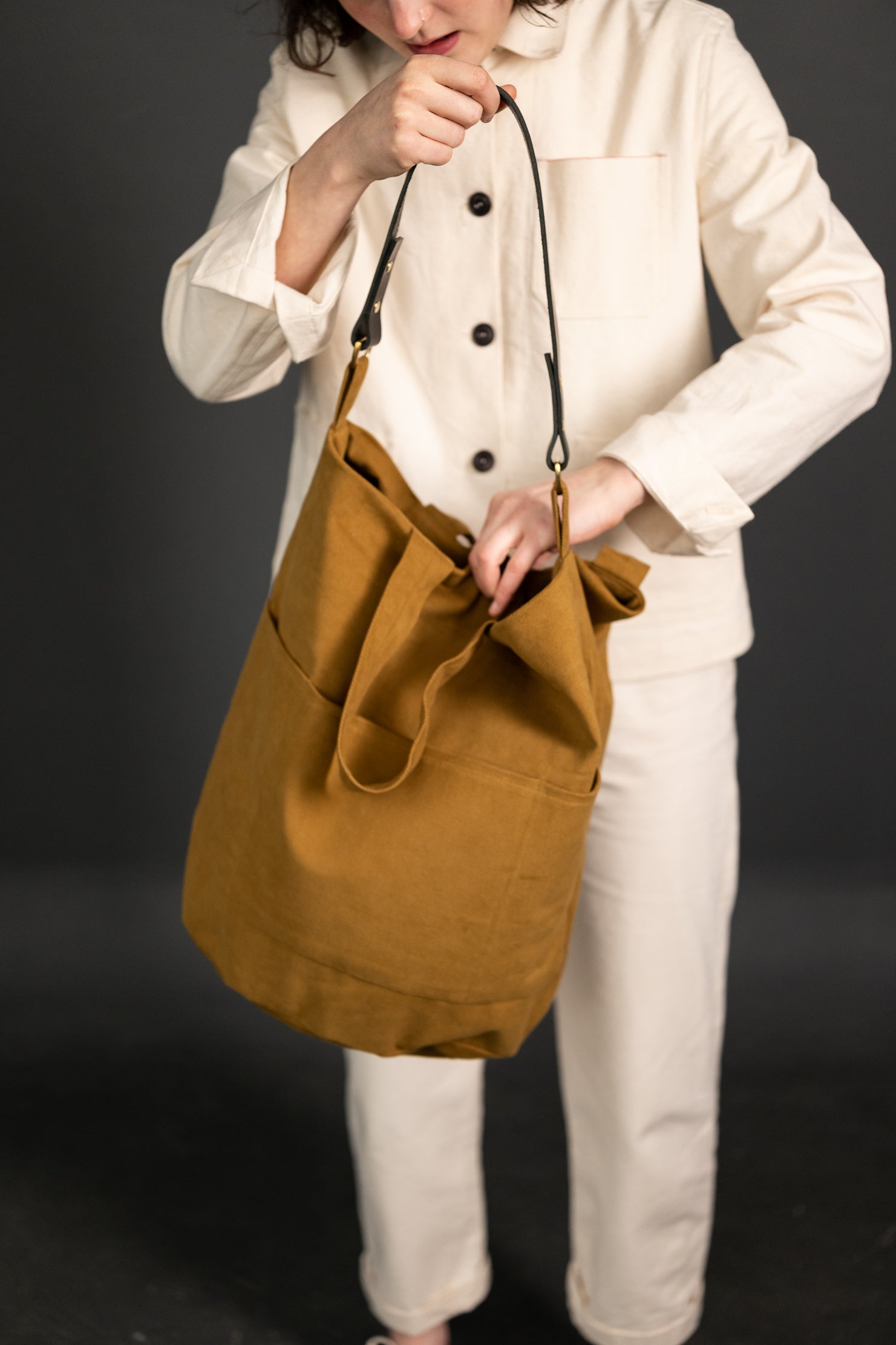 Woman holding The Jack Tar Bag sewing pattern from Merchant & Mills on The Fold Line. A tote bag pattern made in oilskin, sturdy canvas, cotton drill or denim fabrics, featuring three internal pockets, fully lined, fabric handles, leather strap, magnetic