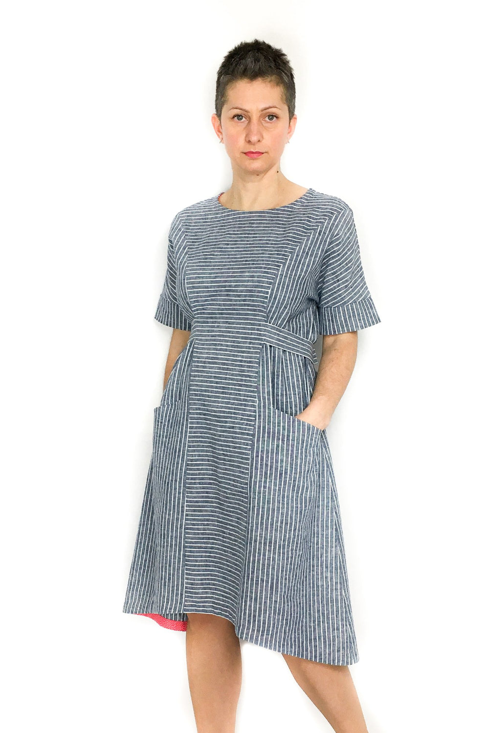 Woman wearing the Jasmine Dress sewing pattern by Dhurata Davies Patterns. A dress pattern made in any light/medium weight woven fabric with some drape, featuring a short sleeve with wide cuff, angled pockets, waist ties and a hem that is slightly raised