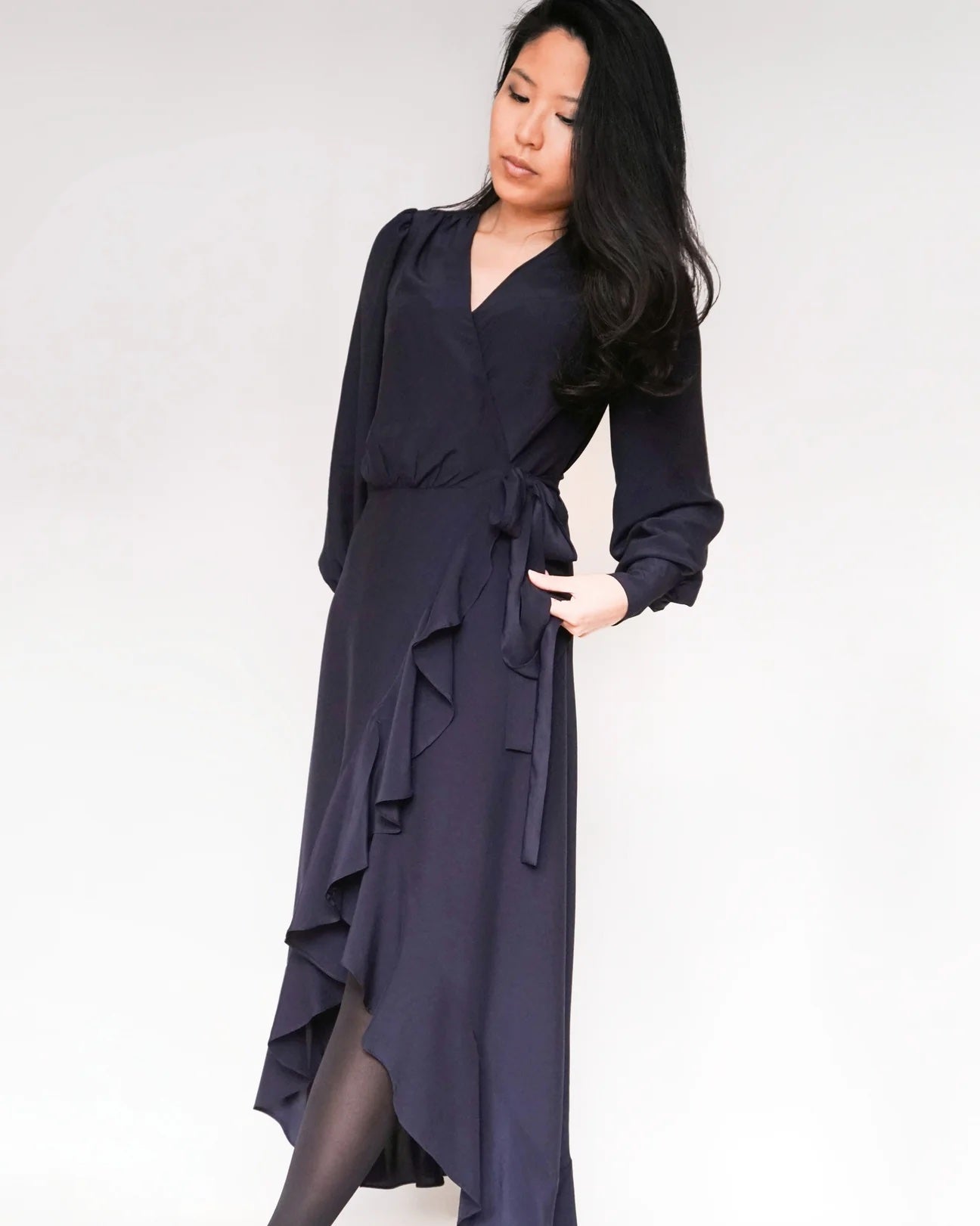Woman wearing the Joline Dress sewing pattern from Bara Studio on The Fold Line. A wrap dress pattern made in viscose, cotton, linen, or lyocell fabrics, featuring a deep V-neck, tiered high-low hem, full length sleeve, gathered cuff with button closure,