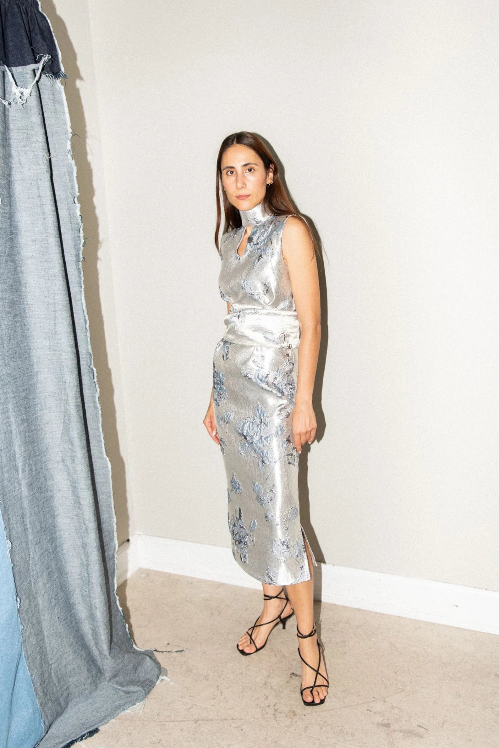 Woman wearing the Keyhole Dress sewing pattern from Puff and Pencil on The Fold Line. A sleeveless dress pattern made in poplin, woven viscose, light denim, silk, or satin fabric, featuring a fitted silhouette, open turtleneck with ties at the back, waist