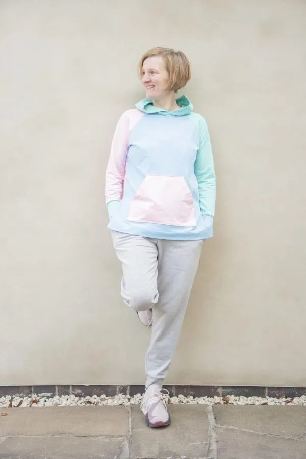 Woman wearing the Lisa Hoodie sewing pattern from Bobbins and Buttons on The Fold Line. A hoodie pattern made in stretch jersey fabrics, featuring a relaxed fit, raglan sleeves, front patch pocket, hood, longline self-fabric cuffs, and deep staggered hem