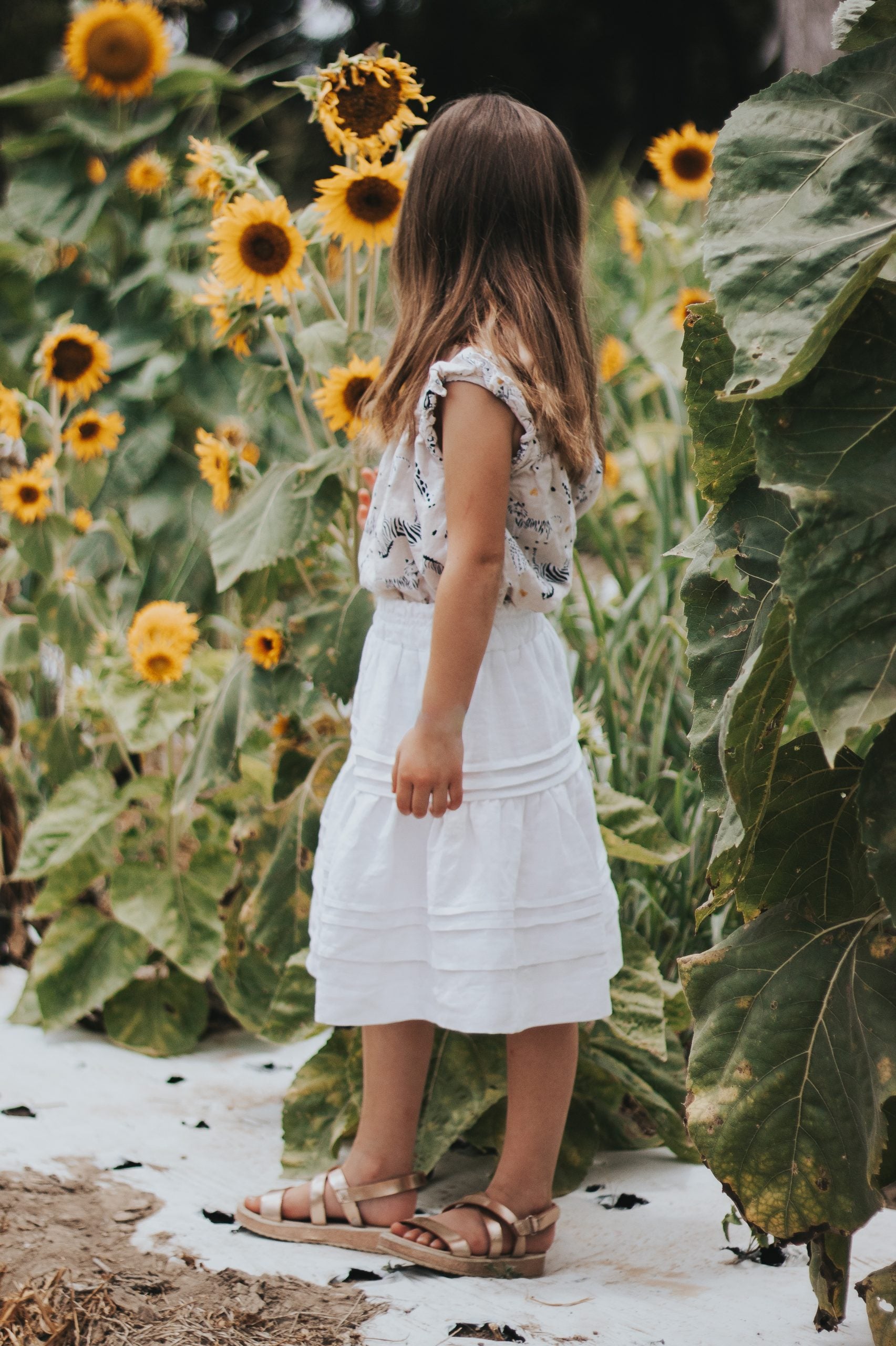 Child wearing the Children's Little Zamora Skirt sewing pattern from Madswick on The Fold Line. A skirt pattern made in cotton, linen or tencel fabrics, featuring an elasticated waist, two gathered tiers, and below knee length.