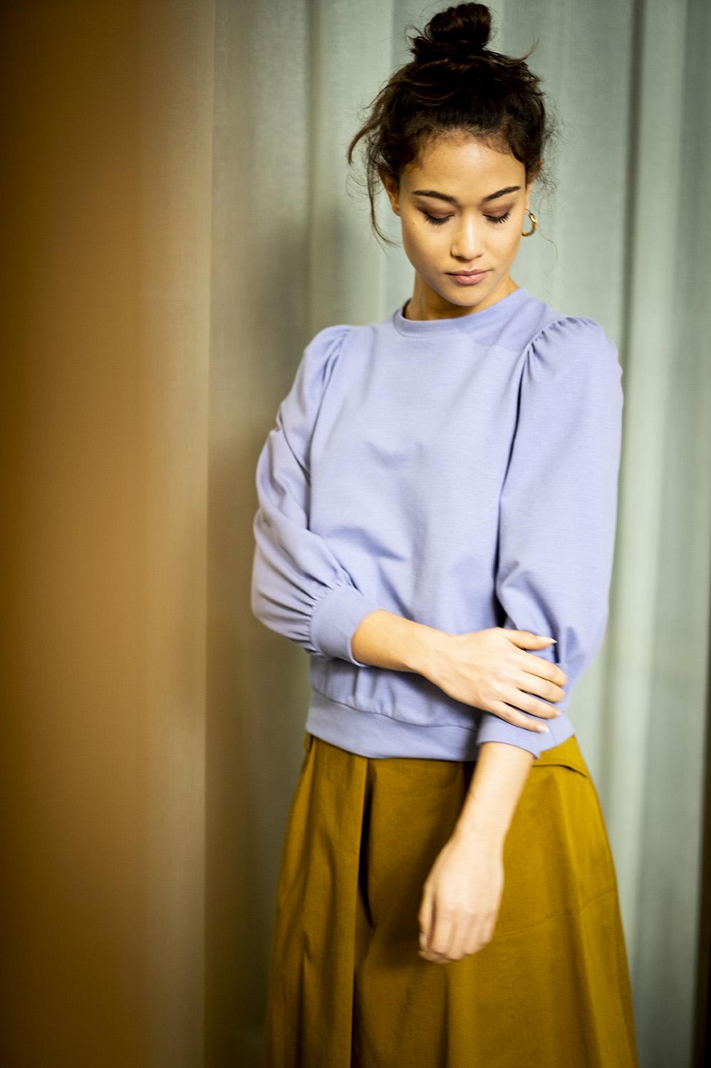 Woman wearing the Mabel Top sewing pattern from Fibre Mood on The Fold Line. A top pattern made in French terry, knit jacquard, sweatshirt fabric or glitter jersey fabrics, featuring a round neckline, 3/4 length puffed sleeves, the neckline, hem and wrist