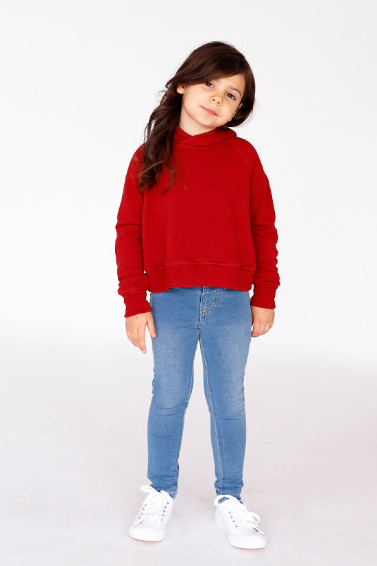 Child wearing the Baby/Child Mini Page Hoodie sewing pattern by Chalk and Notch. A cropped hoodie pattern made in medium weight 50% – 75% stretch knit fabric with good recovery, featuring a banded hem, long sleeves, and draw string hood.