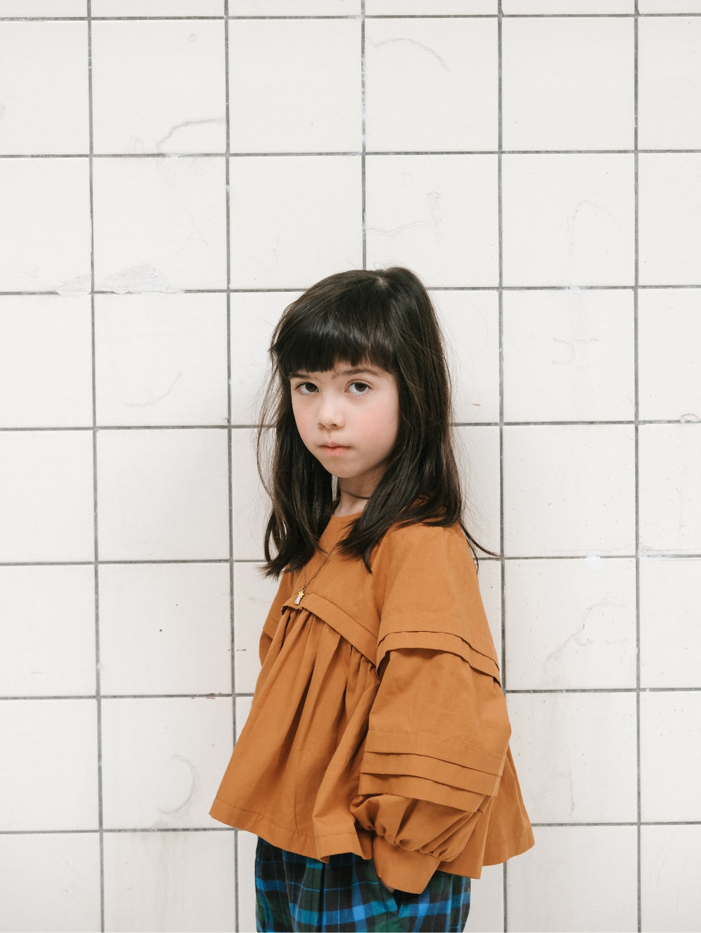 Girl wearing the Child/Teen Didi Blouse sewing pattern from Notches on The Fold Line. A blouse pattern made in cotton poplin, linen, thin wool, or viscose fabric, featuring a round neckline, long lantern sleeve with decorative pleats, and bodice with gath