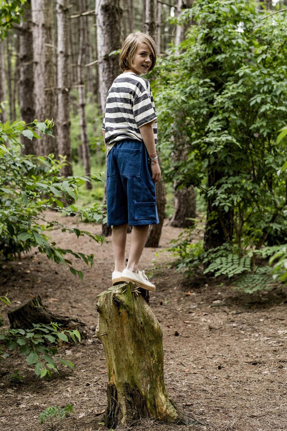 Child wearing the Parker Shorts sewing pattern from Fibre Mood on The Fold Line. A cargo shorts pattern made in poplin, denim or linen fabrics, featuring a knee-length, elasticated waistband, patch pockets, faux fly and angled side pocket.