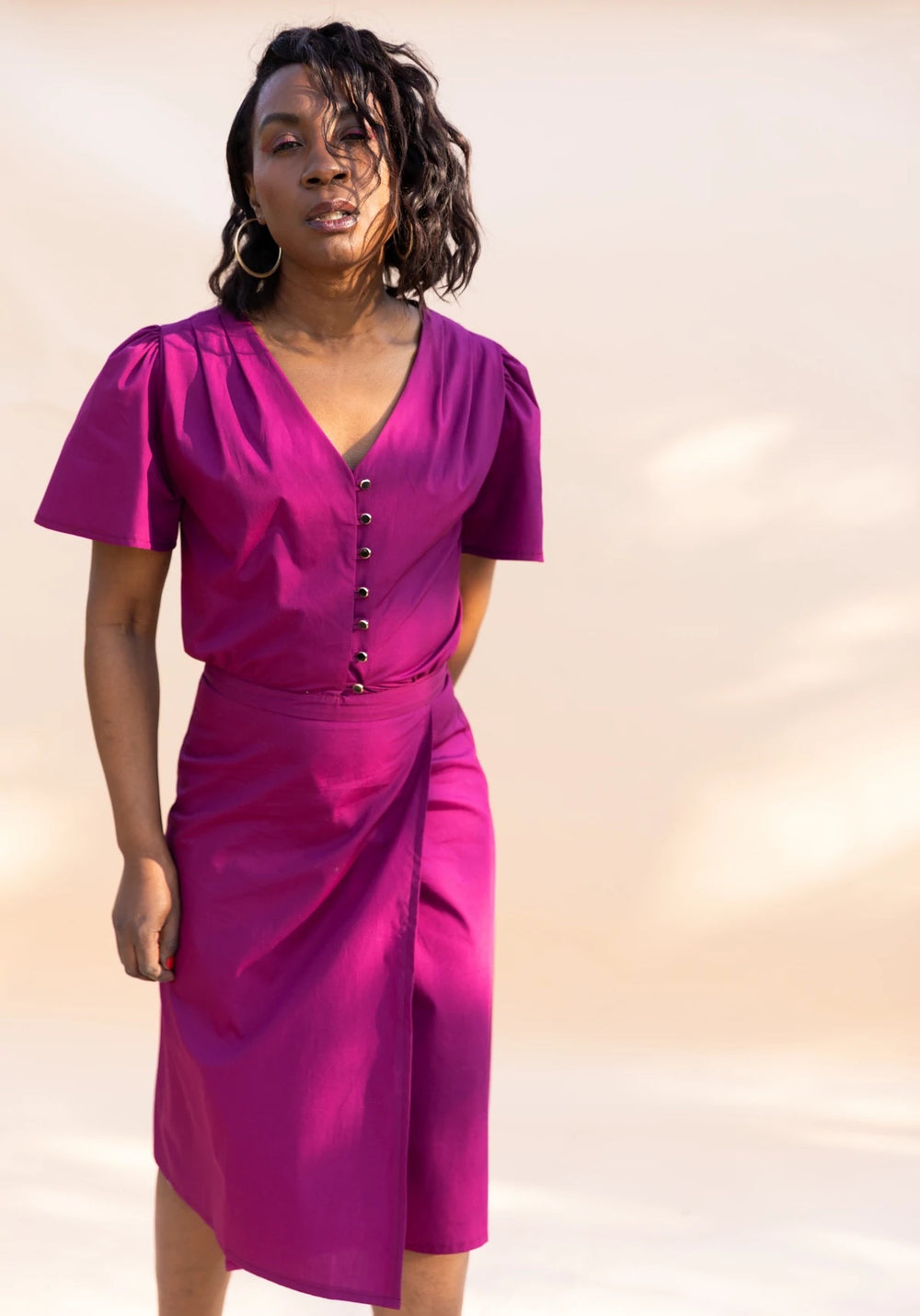 Woman wearing the Penelope Dress sewing pattern from Maison Fauve on The Fold Line. A wrap dress pattern made in viscose, cotton, linen, silk, poplin, crepe or satin fabrics, featuring a buttoned bodice, pleated shoulders, V-neck, short sleeves and below