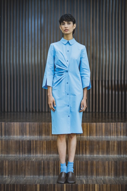 Woman wearing the Phyllis Dress sewing pattern from Fibre Mood on The Fold Line. A shirt dress pattern made in lyocell, poplin, viscose crepe, seersucker, or a fine corduroy fabric, featuring a collar, asymmetric pleats, and 3/4 length sleeves.