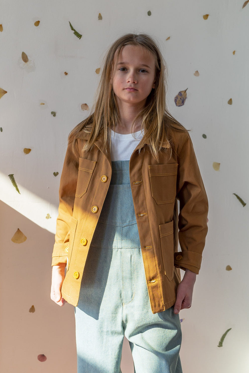 Child wearing the Prosper Bleu de Travail Jacket sewing pattern from Ready to Sew on The Fold Line. A jacket pattern made in denim, cotton canvas, or corduroy fabrics, featuring an unlined straight fit, four patch pockets, topstitching, collar and stand,