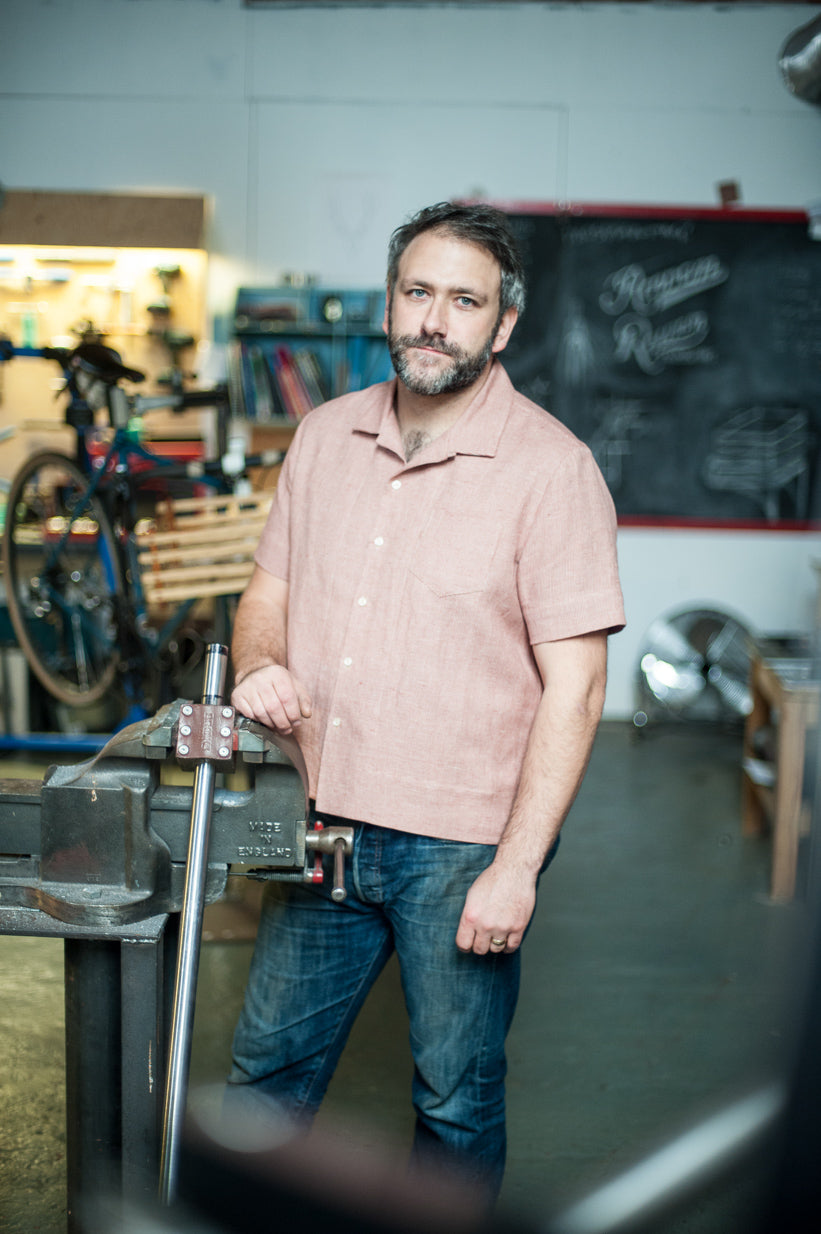 Man wearing the All State Shirt sewing pattern by Merchant and Mills. A short sleeve boxy shirt pattern made in lightweight denims, cotton chambray, linen, corduroy or lightweight wool fabric featuring a one piece collar, patch breast pocket, back yoke an