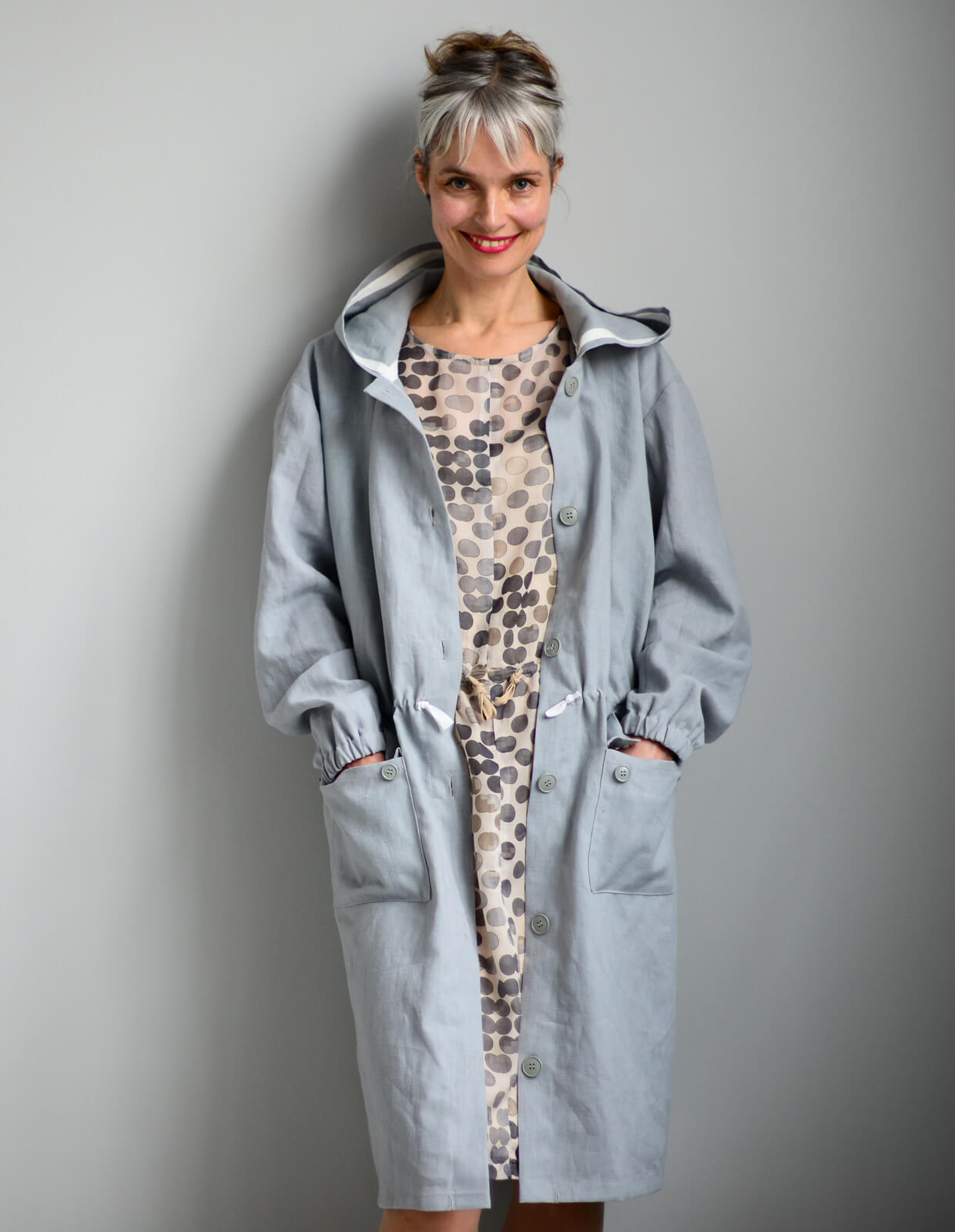 Woman wearing the Utility Coat sewing pattern from The Maker's Atelier on The Fold Line. A coat pattern made in linens, parachute silks, coated or waxed cottons, lightweight waterproof fabrics and oilskins fabrics, featuring a relaxed fit, unlined, hood,