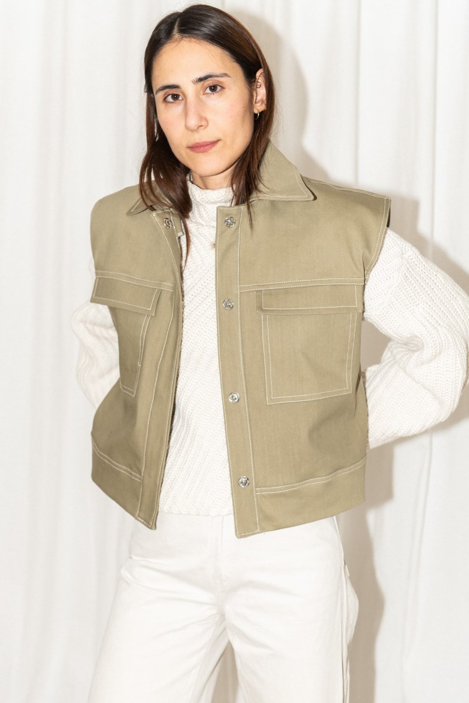 Woman wearing the Topstitch Vest sewing pattern from Puff and Pencil on The Fold Line. A sleeveless vest pattern made in denim or canvas fabric, featuring a boxy fit, collar, drop shoulders, pockets, and snap fasteners.