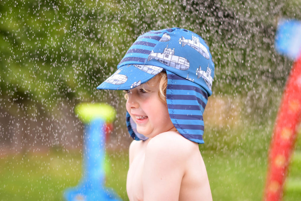 Child wearing the Pool Party Sun Hat sewing pattern from Waves & Wild on The Fold Line. A sun hat pattern made in swim lycra fabrics, featuring a soft hat with peak and neck cover.