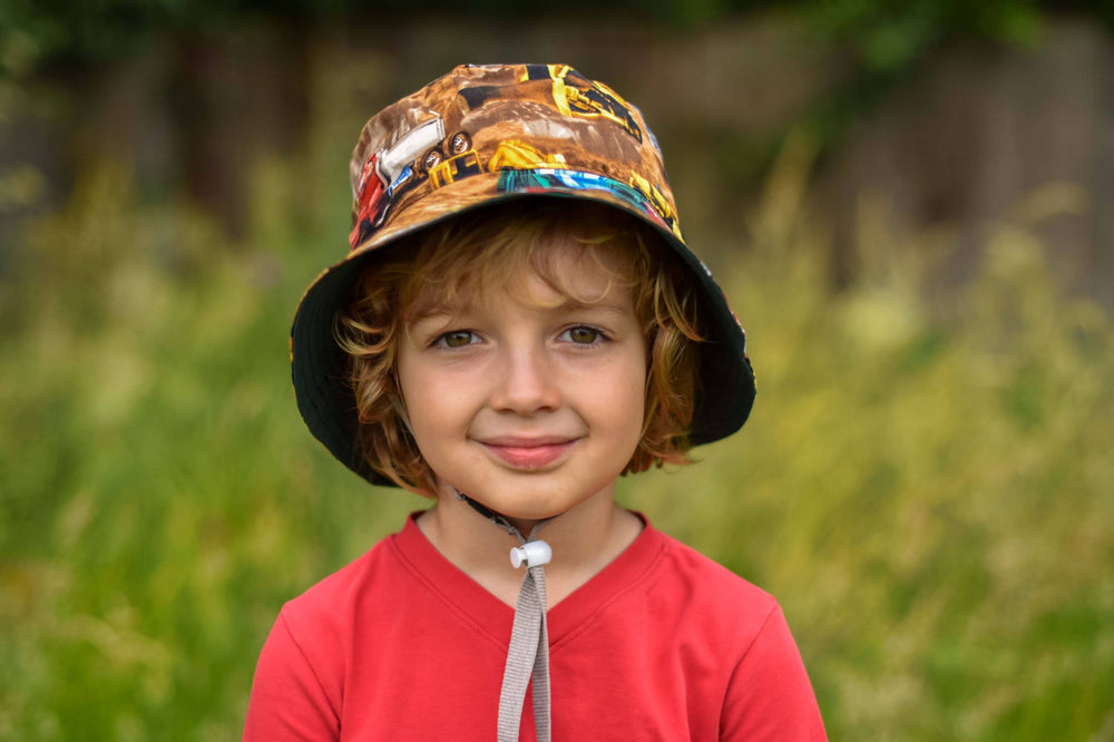 Child wearing the Sandcastle Bucket Hat sewing pattern from Waves & Wild on The Fold Line. A sun hat pattern made in non-stretch light/medium weight woven fabrics, featuring a reversible style, bucket shaped with wide brim.