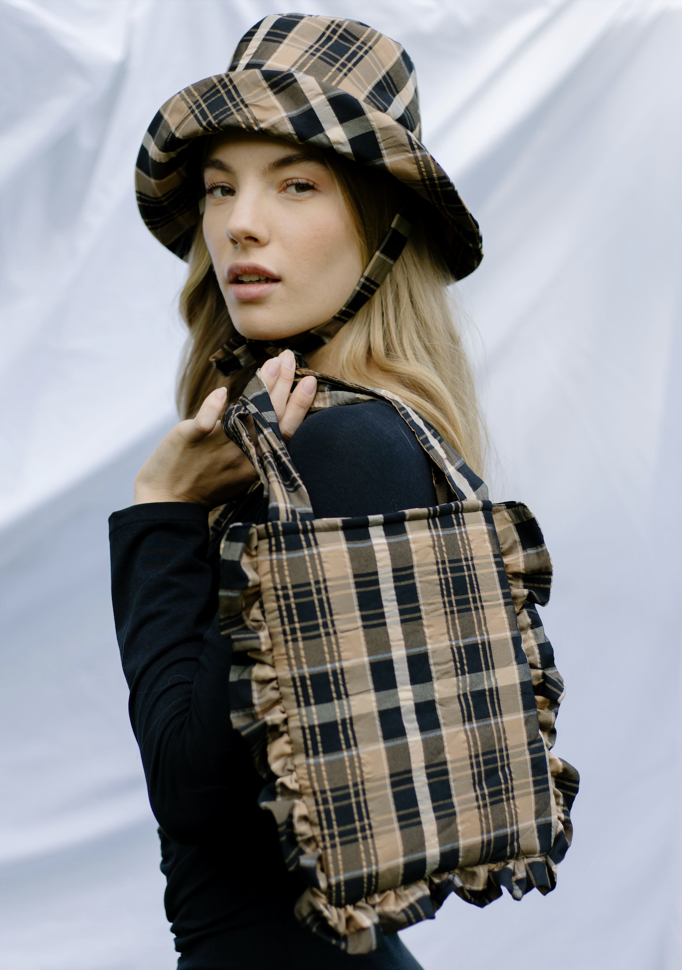Woman holding the Yasmine Bag sewing pattern from JULIANA MARTEJEVS on The Fold Line. A bag pattern made in cotton poplin fabrics, featuring short twin handles, rectangular shape and ruffled edge.