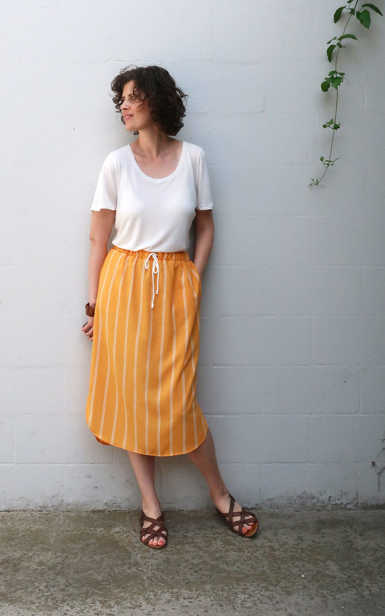 Woman wearing the Lela Skirt sewing pattern from Sew DIY on The Fold Line. A skirt pattern made in chambray, cotton lawn, poplin, rayon, polyester, crepe de chine or georgette fabrics, featuring an elastic waist, straight silhouette, split hem, mid-calf l