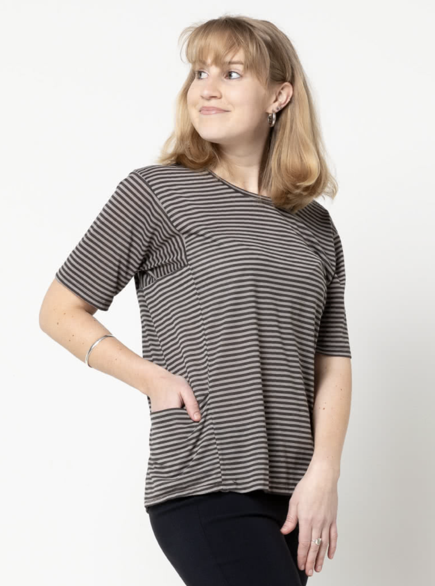 Woman wearing the Ada Knit Top sewing pattern from Style Arc on The Fold Line. A top pattern made in jersey, baby wool or knit fabrics, featuring a boxy silhouette, round neck, short sleeves, square-shaped armholes, and slightly draped pockets inserted in